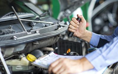 Hand holding a flashlight and instructions while investigating an auto engine. West Financial Services