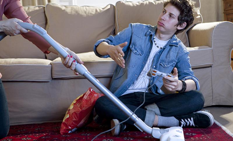 Teen looking at his mom vacuuming. West Financial Services, Inc.