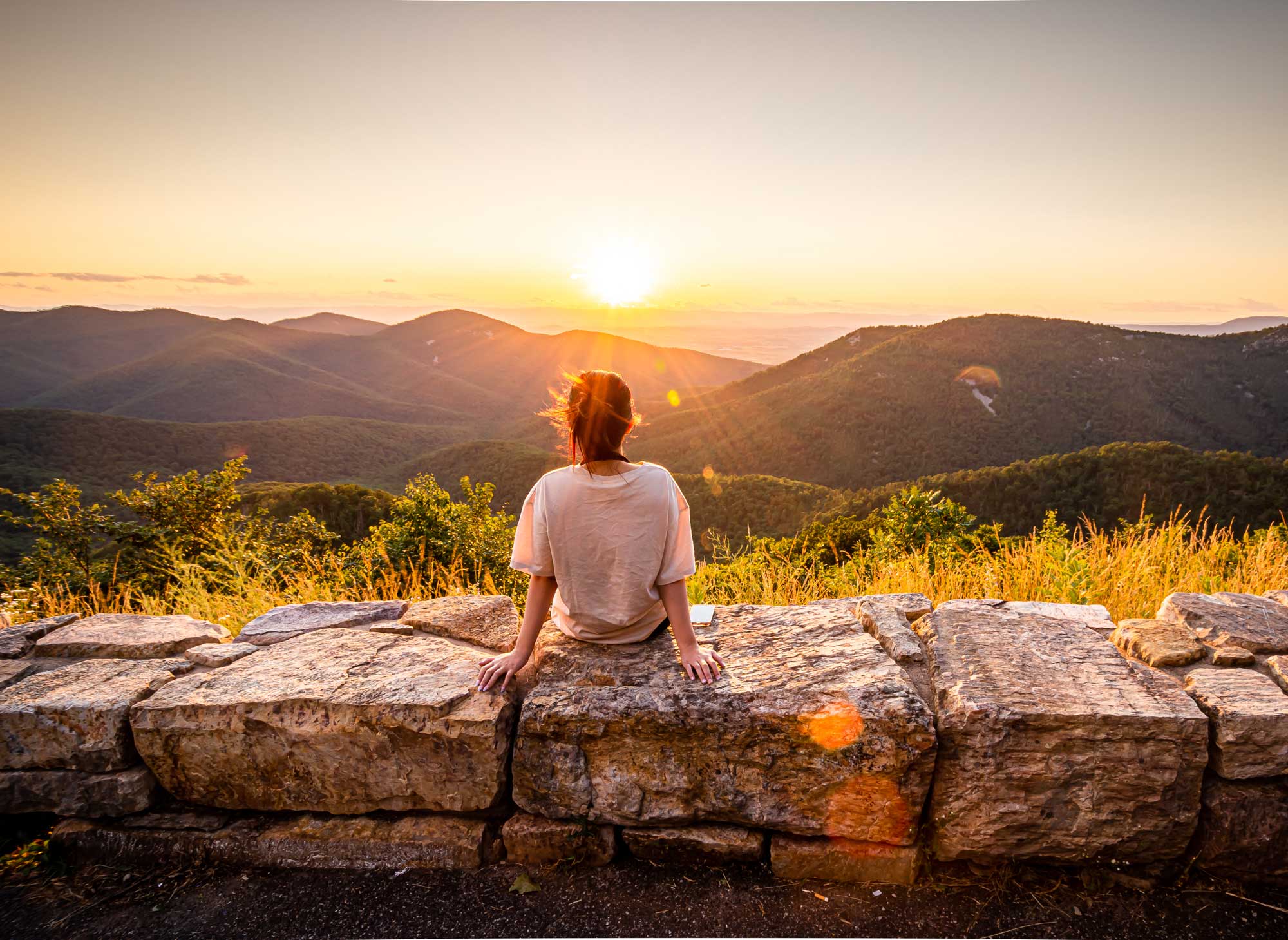 person looking into distance on top of valley sunset