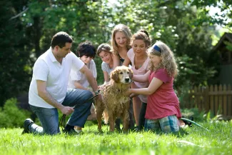 Family gathered outside on a sunny day giving a bath to their golden retriever, smiling and enjoying the activity together.
