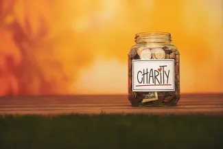 Glass jar labeled “Charity” filled with coins and cash, placed on a wooden surface with a warm orange background symbolizing generosity and giving.