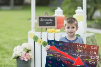 Kid in front of a lemonade stand. Kid holding price chart. West Financial Services.