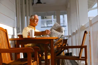 Man on his front porch reading a newspaper. West Financial Services.