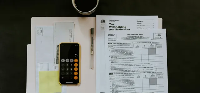 Tax documents, a folder, smartphone calculator, pen, and a cup of coffee arranged neatly on a dark table.