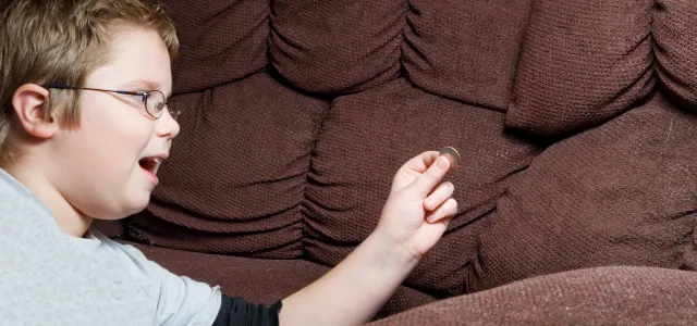 Young boy smiling while holding a coin he found between the cushions of a brown couch.