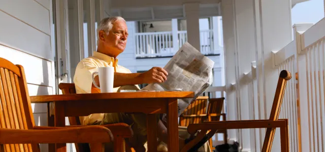 Man on his front porch reading a newspaper. West Financial Services.